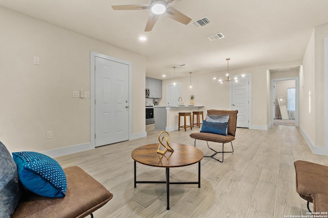 living room featuring light hardwood / wood-style flooring, ceiling fan with notable chandelier, and sink