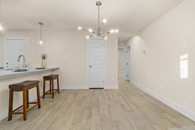 kitchen featuring light stone countertops, a kitchen breakfast bar, decorative light fixtures, light hardwood / wood-style flooring, and a notable chandelier