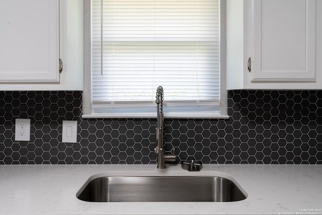 interior details featuring backsplash, light stone counters, white cabinetry, and sink