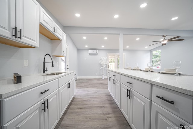 kitchen with light wood-type flooring, light stone counters, sink, an AC wall unit, and white cabinetry