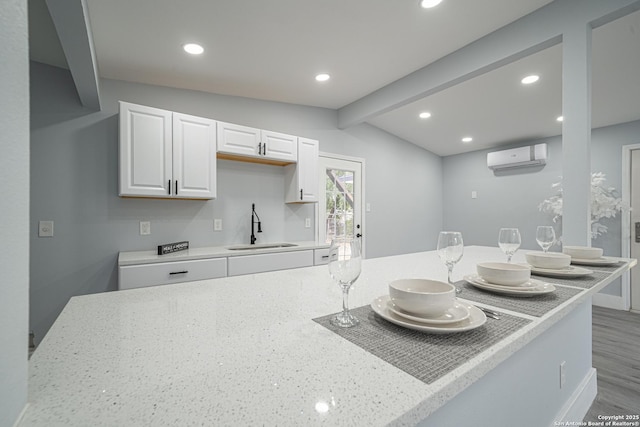 kitchen with light stone countertops, a wall mounted AC, sink, vaulted ceiling with beams, and white cabinetry