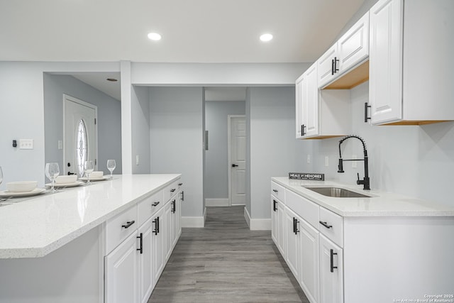 kitchen with white cabinetry, sink, light stone countertops, and light hardwood / wood-style flooring