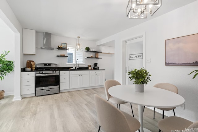 kitchen with white cabinets, sink, wall chimney exhaust hood, decorative light fixtures, and stainless steel range oven