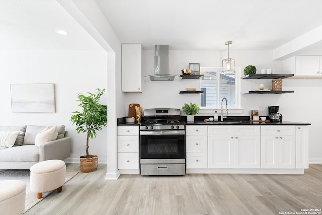 kitchen featuring wall chimney range hood, sink, light hardwood / wood-style floors, white cabinetry, and gas stove