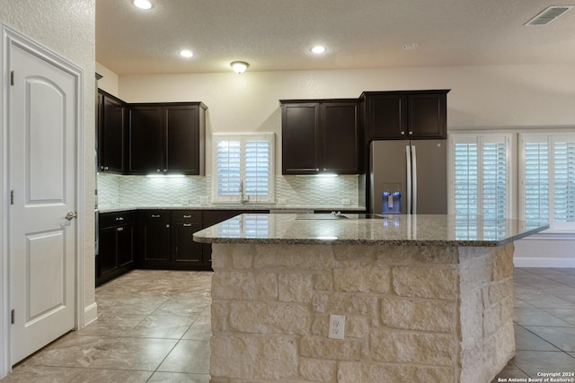 kitchen with tasteful backsplash, light stone countertops, a center island, and stainless steel refrigerator with ice dispenser