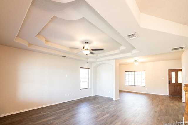 spare room with plenty of natural light, ceiling fan, dark wood-type flooring, and a tray ceiling