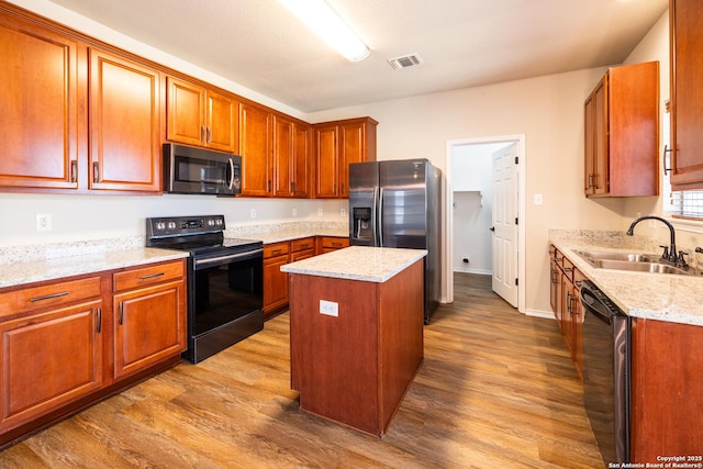 kitchen featuring sink, a kitchen island, light stone countertops, appliances with stainless steel finishes, and light hardwood / wood-style floors