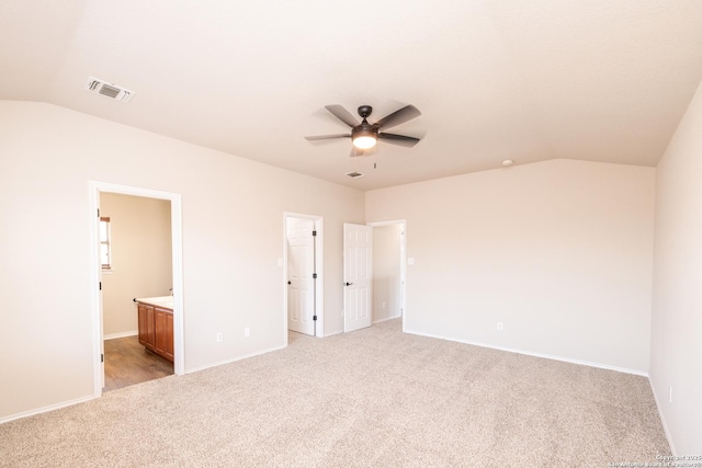 unfurnished bedroom featuring vaulted ceiling, light colored carpet, ensuite bath, and ceiling fan