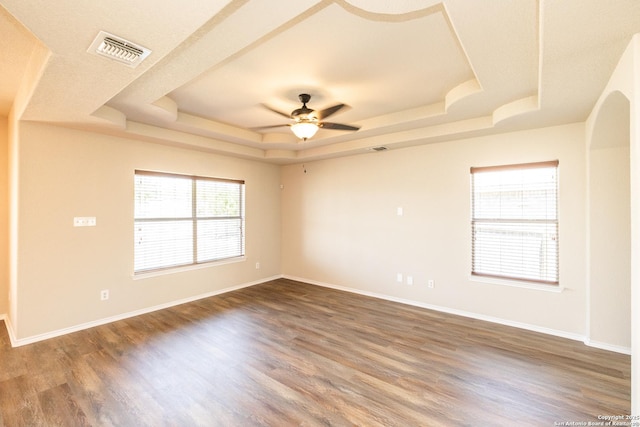 spare room with a tray ceiling, ceiling fan, and dark wood-type flooring