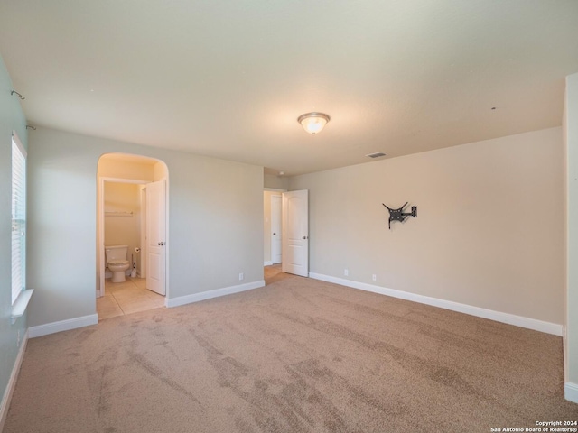 unfurnished bedroom featuring light colored carpet, ensuite bath, and a spacious closet