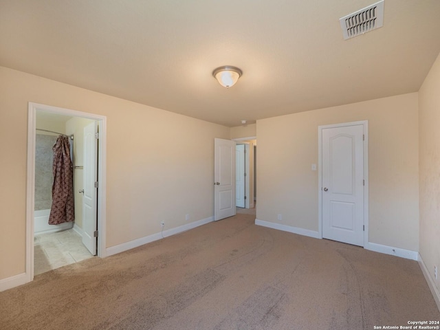 unfurnished bedroom featuring light carpet, ensuite bathroom, and a closet