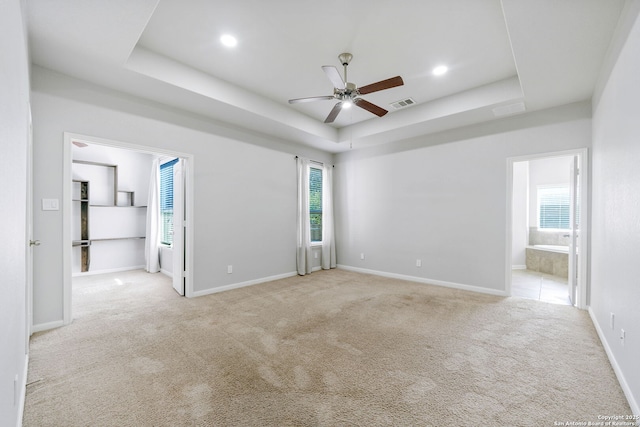 spare room with ceiling fan, a raised ceiling, and light colored carpet