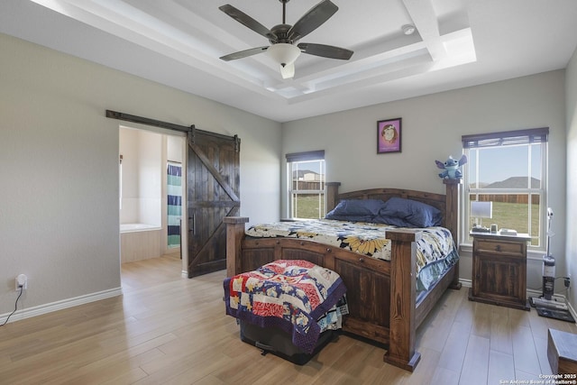 bedroom featuring a barn door, ensuite bath, light hardwood / wood-style flooring, and ceiling fan