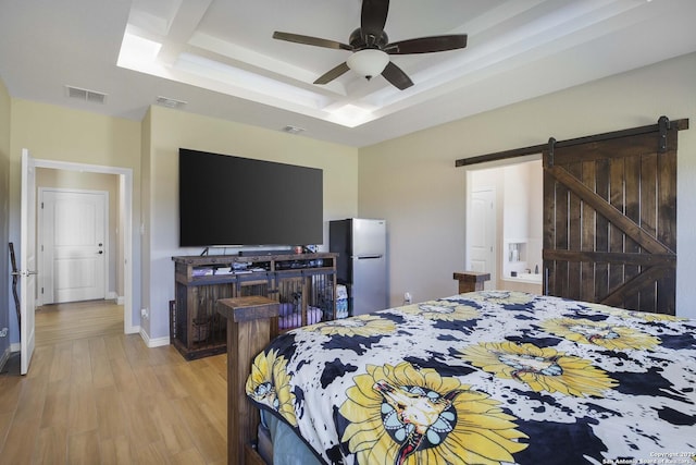 bedroom featuring a raised ceiling, ceiling fan, a barn door, light hardwood / wood-style floors, and stainless steel refrigerator