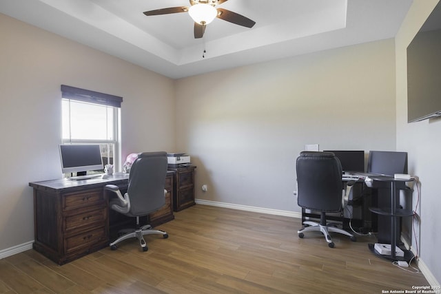 office space featuring light wood-type flooring, a tray ceiling, and ceiling fan