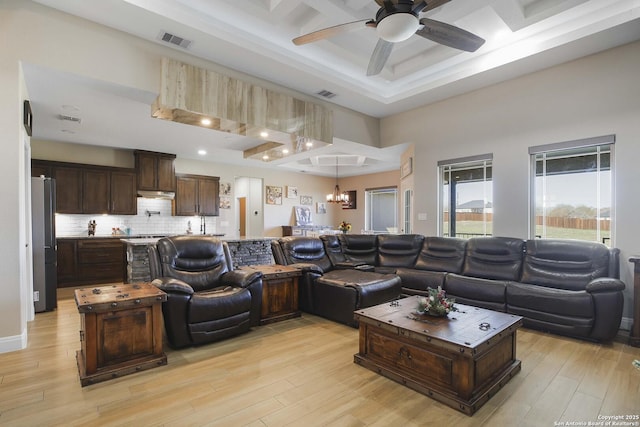 living room with ceiling fan with notable chandelier, light hardwood / wood-style floors, and coffered ceiling