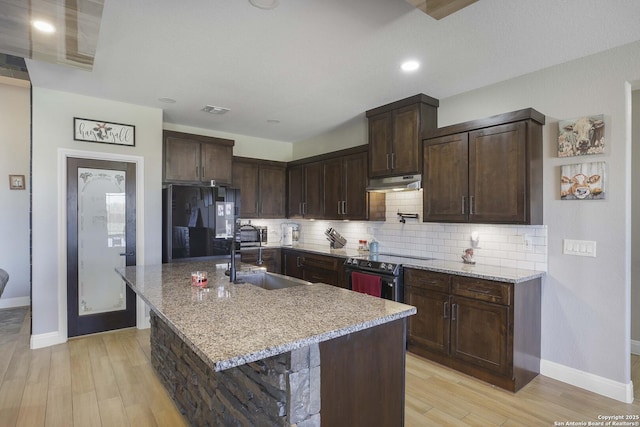 kitchen with backsplash, black fridge, an island with sink, electric range oven, and light stone counters