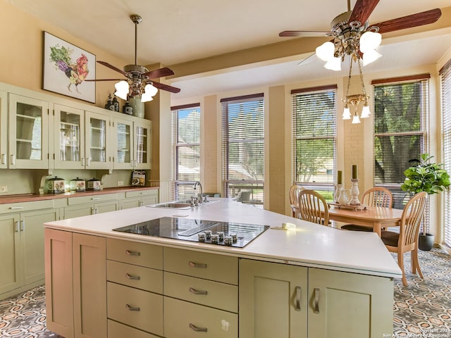 kitchen with black electric cooktop, sink, an island with sink, and ceiling fan with notable chandelier