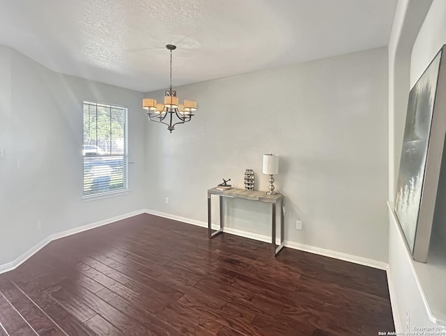 empty room featuring a textured ceiling, dark wood-type flooring, and an inviting chandelier