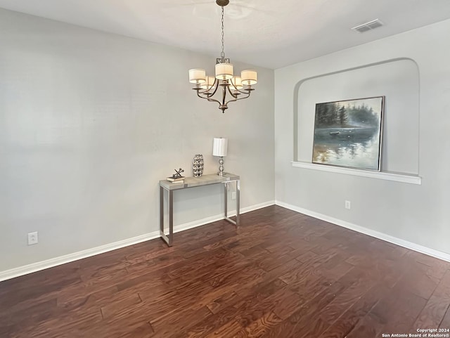 spare room with dark hardwood / wood-style flooring and a chandelier