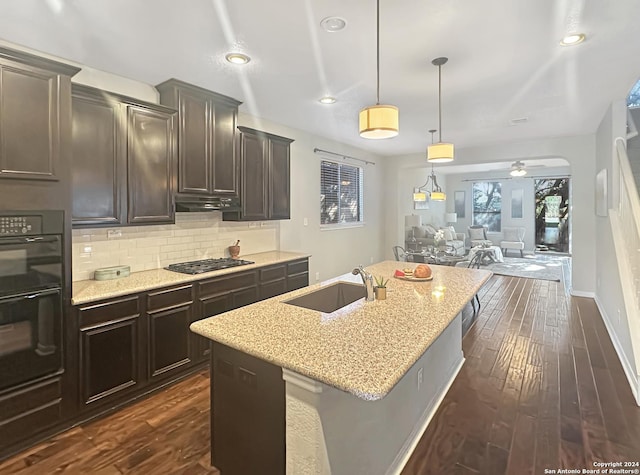 kitchen with light stone countertops, ceiling fan, sink, hanging light fixtures, and an island with sink