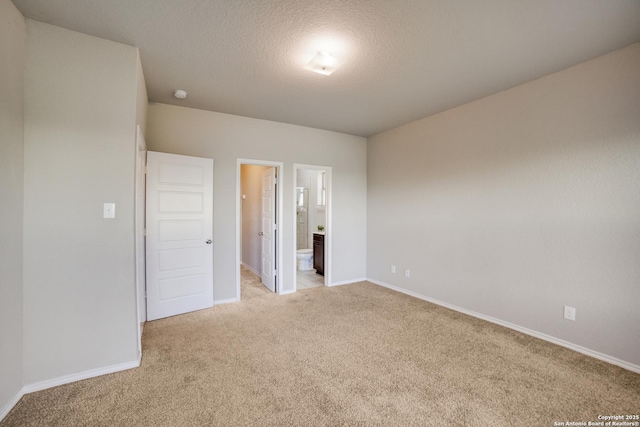 unfurnished bedroom with light carpet, a textured ceiling, and ensuite bath