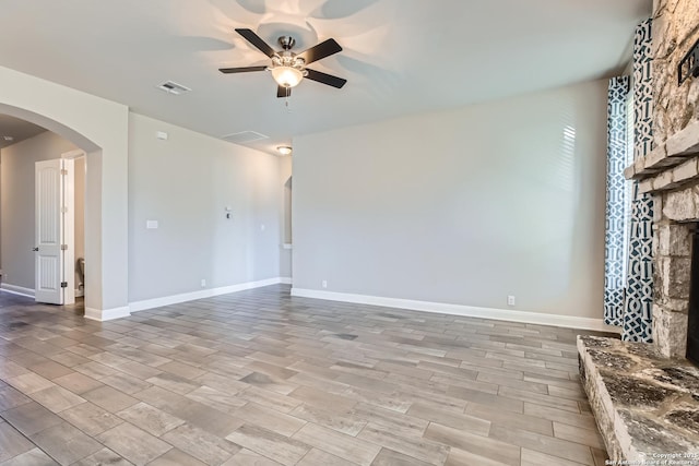 unfurnished living room with ceiling fan and a stone fireplace