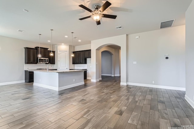 kitchen with sink, decorative light fixtures, an island with sink, ceiling fan, and decorative backsplash