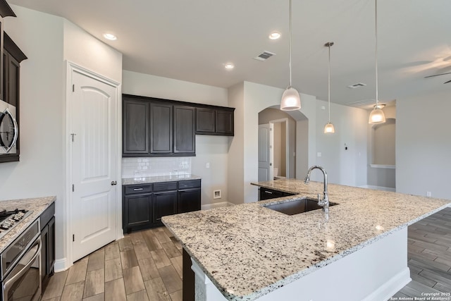 kitchen with sink, hanging light fixtures, a large island, light stone countertops, and decorative backsplash