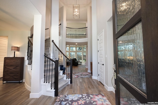 entryway featuring a notable chandelier, wood-type flooring, and a towering ceiling