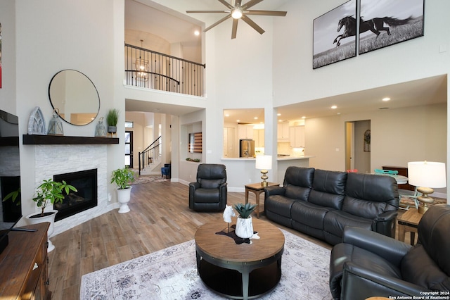 living room with a stone fireplace, ceiling fan, a towering ceiling, and hardwood / wood-style flooring