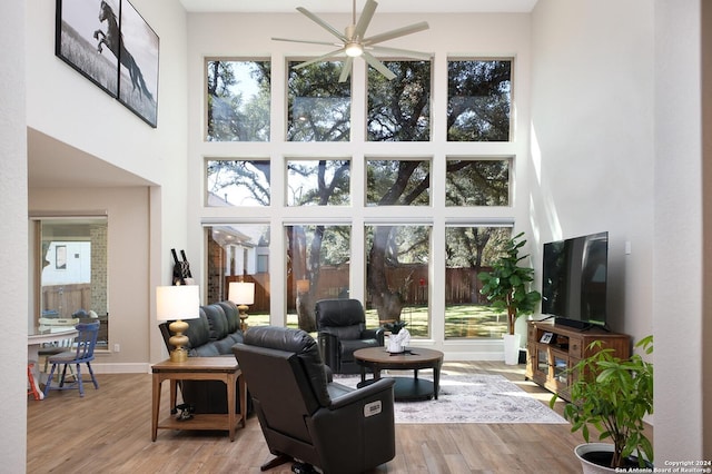 living room with ceiling fan, a healthy amount of sunlight, a high ceiling, and light hardwood / wood-style flooring