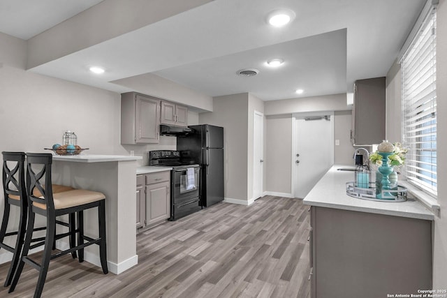 kitchen featuring light hardwood / wood-style floors, sink, black appliances, gray cabinets, and a breakfast bar area