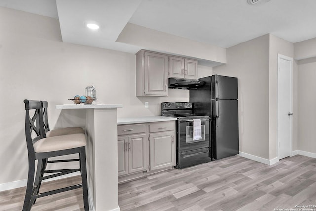 kitchen featuring black appliances, light hardwood / wood-style floors, gray cabinetry, and a breakfast bar area