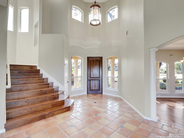 foyer with a high ceiling, decorative columns, an inviting chandelier, and light tile patterned flooring