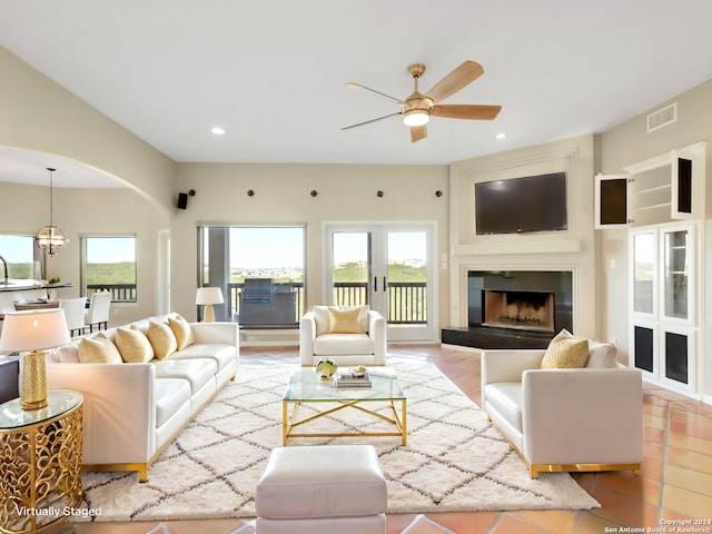 tiled living room with a tile fireplace, french doors, ceiling fan with notable chandelier, and sink