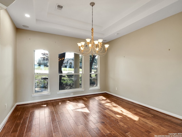 unfurnished dining area with a raised ceiling, hardwood / wood-style floors, and an inviting chandelier