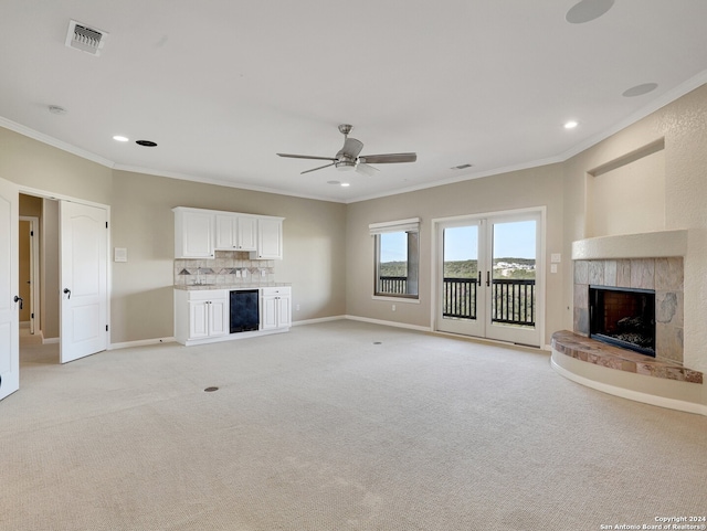 unfurnished living room featuring ceiling fan, beverage cooler, crown molding, light carpet, and a fireplace