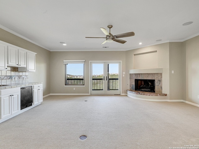 unfurnished living room with ceiling fan, light colored carpet, ornamental molding, and a fireplace