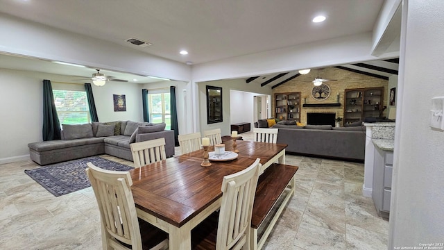 dining area featuring vaulted ceiling with beams, ceiling fan, and a large fireplace