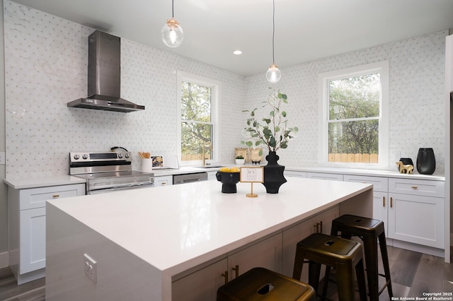 kitchen featuring a center island, wall chimney range hood, appliances with stainless steel finishes, decorative light fixtures, and white cabinetry