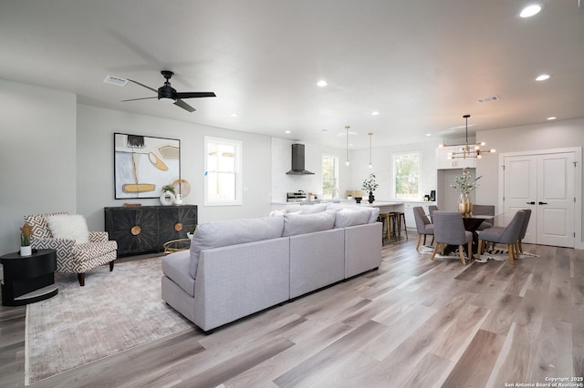 living room with ceiling fan with notable chandelier, a healthy amount of sunlight, and light hardwood / wood-style flooring