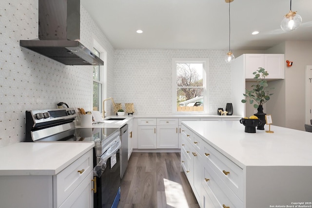 kitchen with dark wood-type flooring, wall chimney range hood, pendant lighting, white cabinets, and appliances with stainless steel finishes