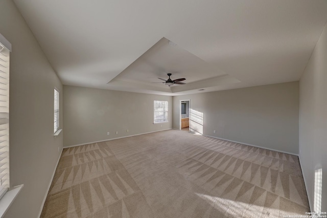 unfurnished room featuring light carpet, a tray ceiling, and ceiling fan