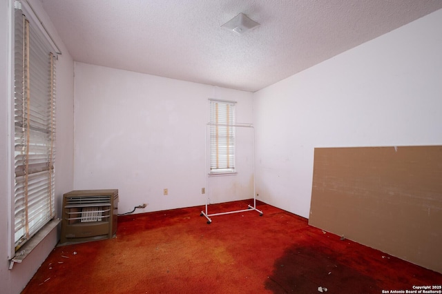 unfurnished bedroom with carpet flooring, heating unit, and a textured ceiling