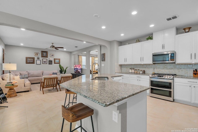 kitchen featuring appliances with stainless steel finishes, a kitchen breakfast bar, a kitchen island with sink, sink, and white cabinets