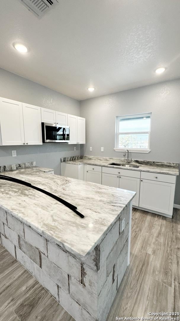 kitchen featuring light stone countertops, light hardwood / wood-style floors, white cabinetry, and sink