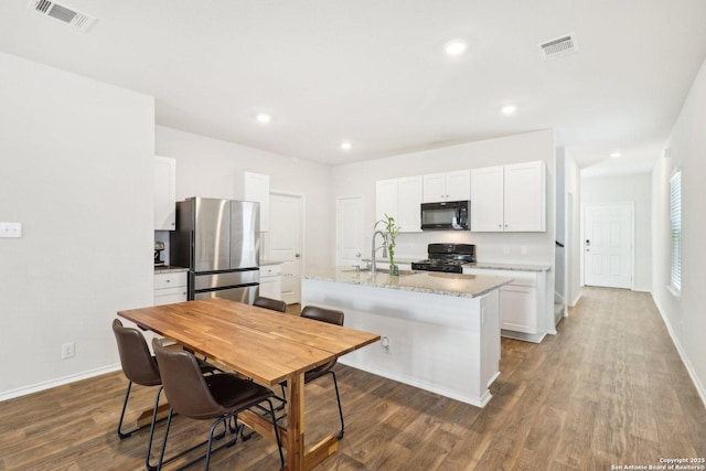 kitchen with light stone countertops, dark wood-type flooring, a center island with sink, white cabinets, and black appliances