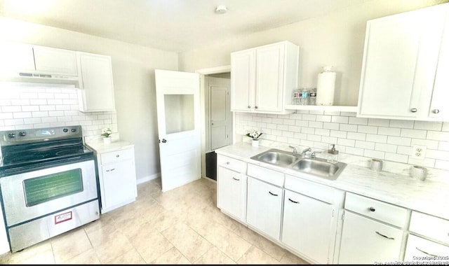 kitchen with stainless steel range with electric stovetop, backsplash, sink, light tile patterned floors, and white cabinetry