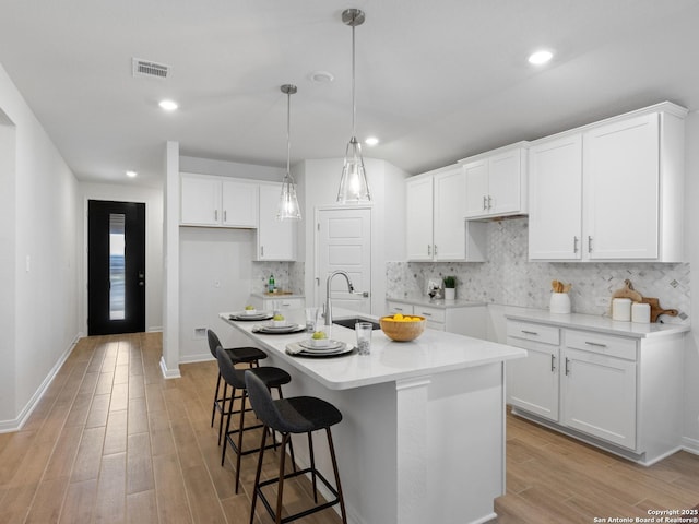 kitchen featuring tasteful backsplash, a kitchen island with sink, sink, white cabinets, and hanging light fixtures